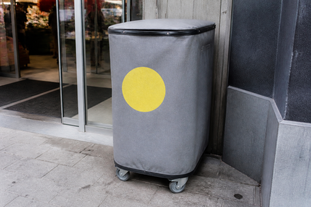 Grijze textielbak met gele sticker naast supermarktingang